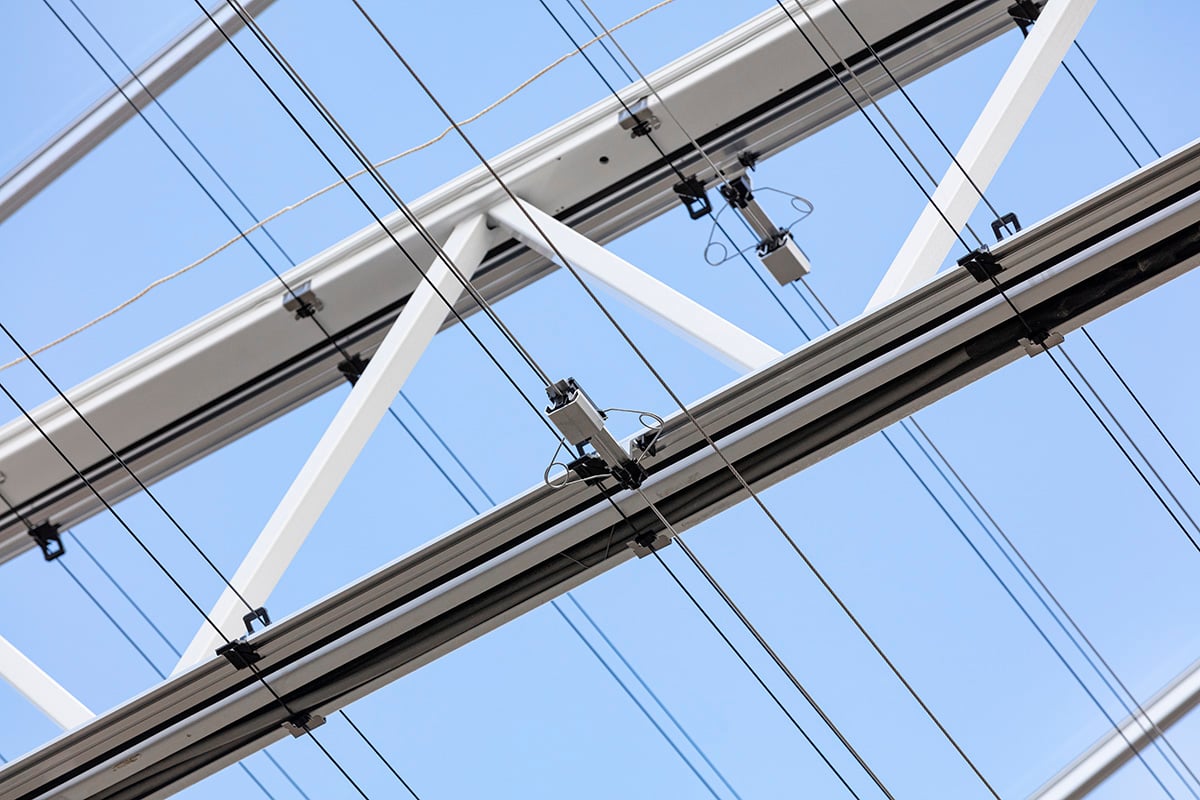 An overhead electricity infrastructure with multiple cross beams and power lines against a clear blue sky.