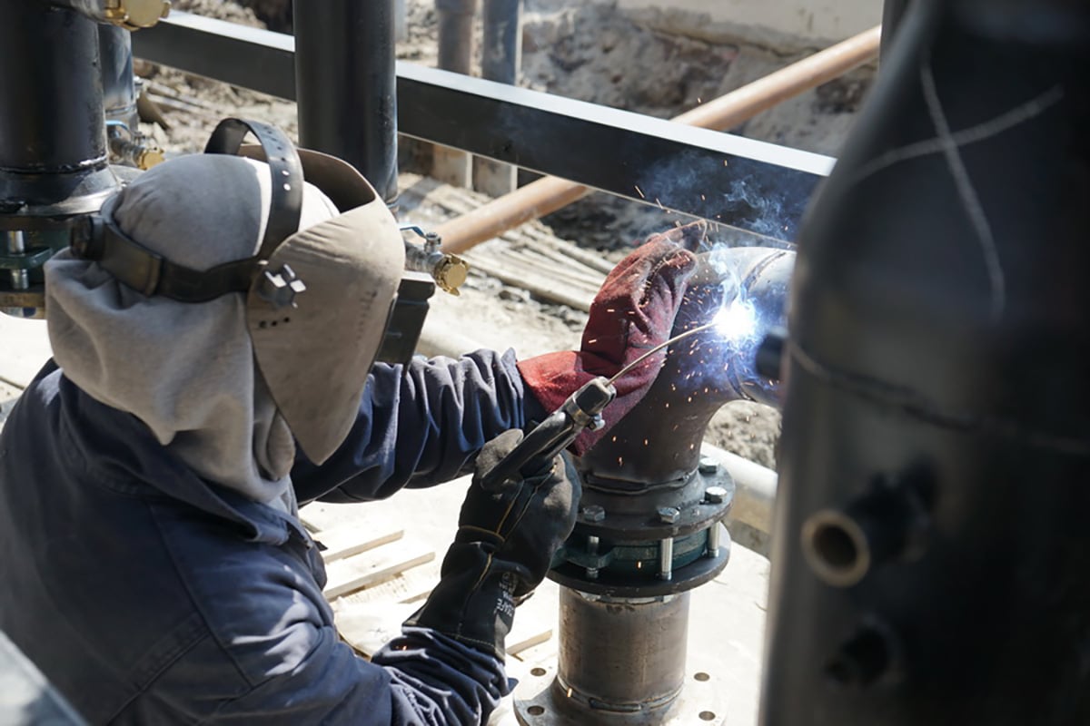 A person wearing a helmet and gloves, working with a welding torch on a piece of metal.